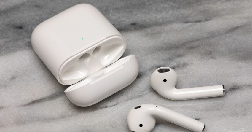 The second-generation AirPods near their charging case on a white surface.