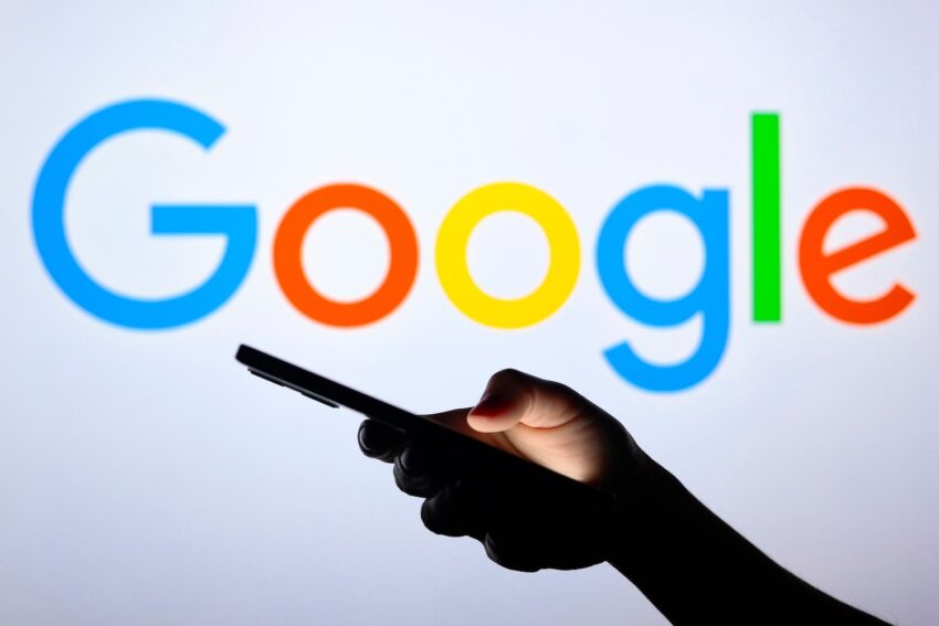 Google's logo is shown behind a silhouette hand holding a smartphone.